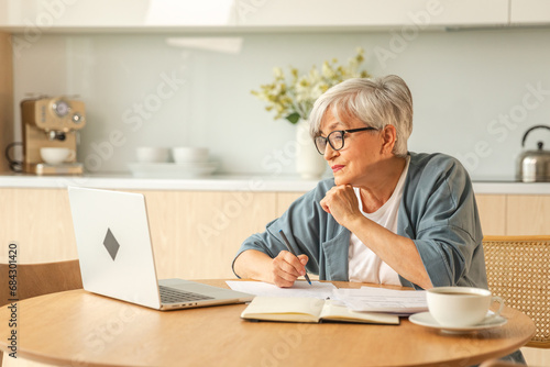 Online education courses webinar concept. Middle aged senior woman using laptop computer writing notes. Focused mature old woman enjoying studying online from home written records doing online work photo