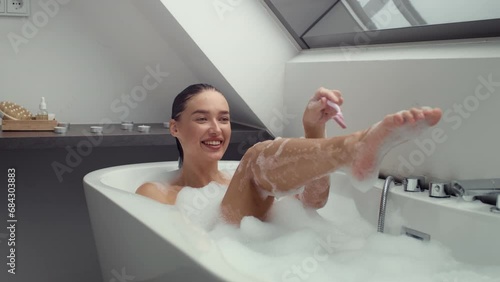 4K slow-motion footage of happy woman in foamy bath shaving legs photo