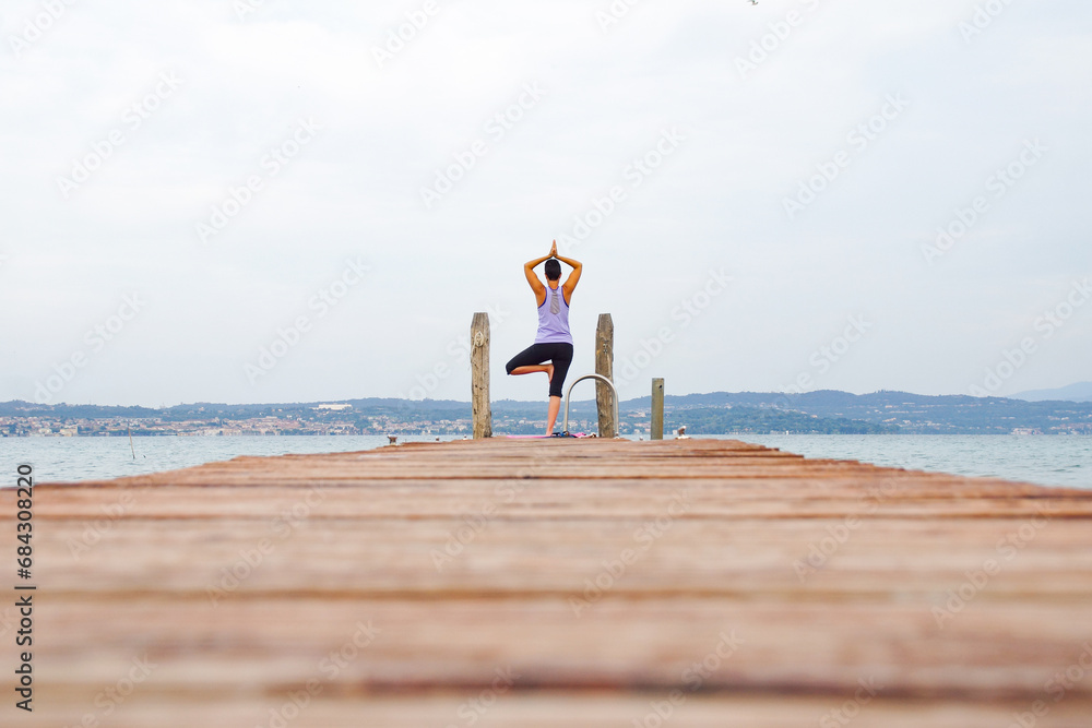 woman makes yoga on the wooden pier of a lake