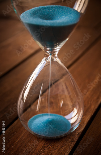 Hourglass containing blue sand on a rustic wooden board