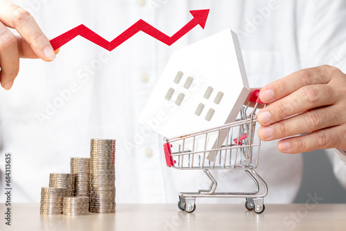 Tableau sur toile Businessman hand hold the arrow graph with growing value and a shopping cart and home and stack coin with growing interest in the office, Loan for real estate or saving money for buy a house concept