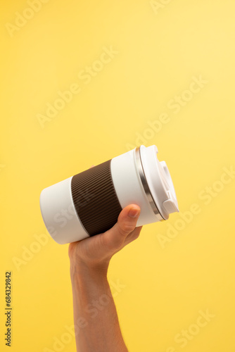 Fototapeta Naklejka Na Ścianę i Meble -  Hand of a girl taking a thermos of coffee on a yellow background. copy space