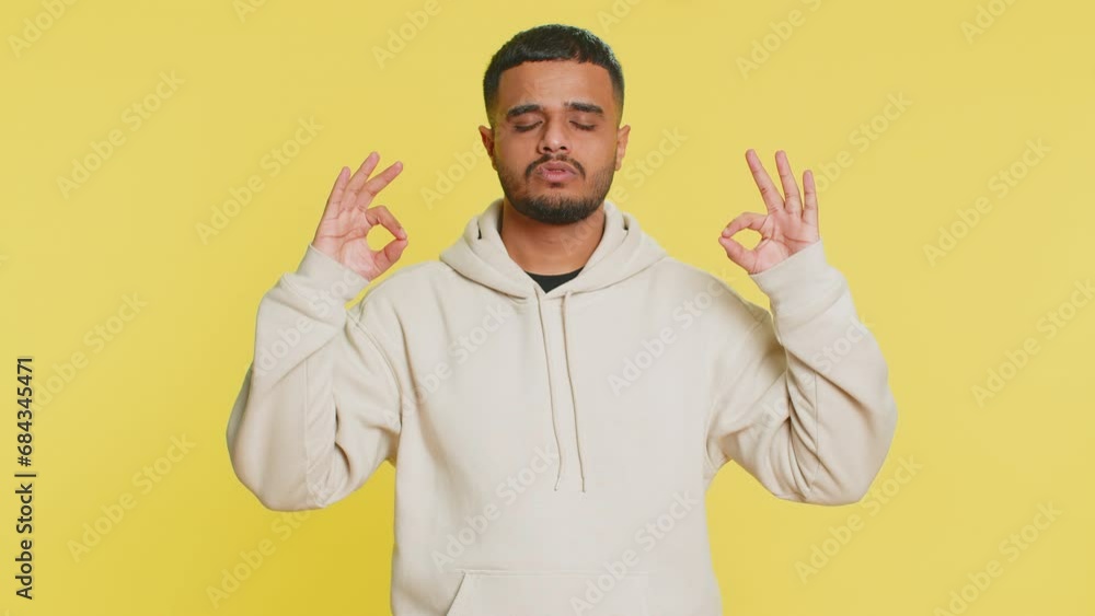 Keep calm down, relax, rest. Concentrated happy Indian man meditating breathes deeply with mudra yoga gesture, eyes closed, peaceful mind, taking a break. Arabian Hindu guy on yellow studio background Keep calm down, relax, rest. Concentrated happy Indian man meditating breathes deeply with mudra yoga gesture, eyes closed, peaceful mind, taking a break. Arabian Hindu guy on yellow studio background