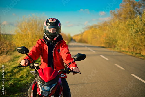 Fototapeta Naklejka Na Ścianę i Meble -  Biker girl on a motorcycle rides on an empty asphalt road outside the city.