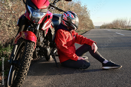 young attractive biker girl in red sitting next to her red motorcycle in the middle of the road. biker with a motorcycle outside the city.