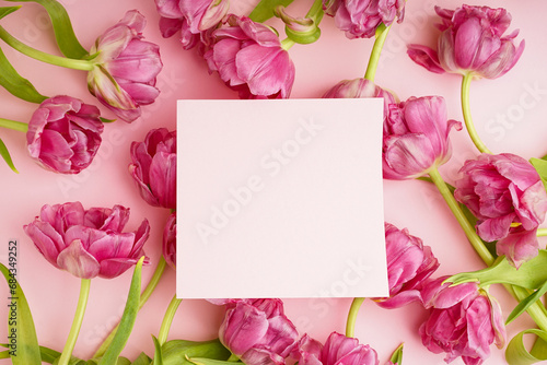 Festive concept for Mother's Day or Valentines Day. Beautiful bouquet of pink peony tulips and a card in the middle on a pink background with space for text. Top view.