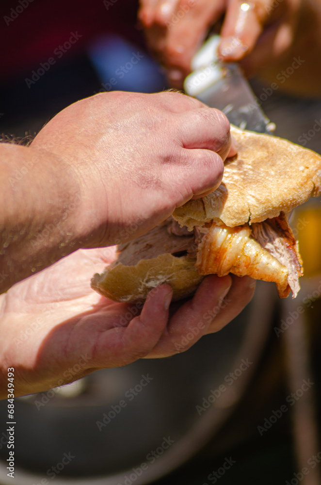 hand holding meat between two pieces of bread to make a Bifana, a typical Portuguese meat sandwich.