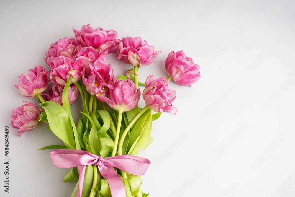 Bouquet of pink peony tulips tied with a pink bow. Spring flowers on the white background and place for text. Festive concept for Valentines Day or Mother's Day.
