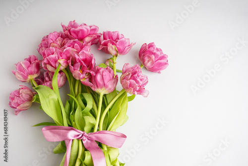 Bouquet of pink peony tulips tied with a pink bow. Spring flowers on the white background and place for text. Festive concept for Valentines Day or Mother s Day.