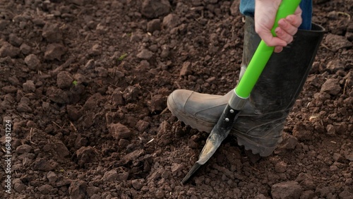 Farmer, gardener, man, woman in rubber boots dig earth with shovel in garden, in field, on farm. Concept of organic farming. Farmer dig soil in garden with shovel, digs grass with a shovel. Gardening