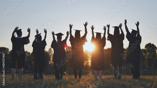 College graduates in robes waving at sunset.