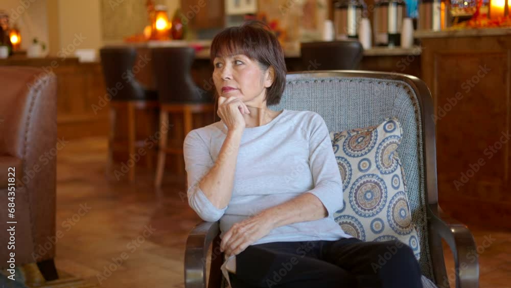 Beautiful mature woman relaxing looking around lobby relaxing sitting in comfortable chair Beautiful mature woman relaxing looking around lobby relaxing sitting in comfortable chair