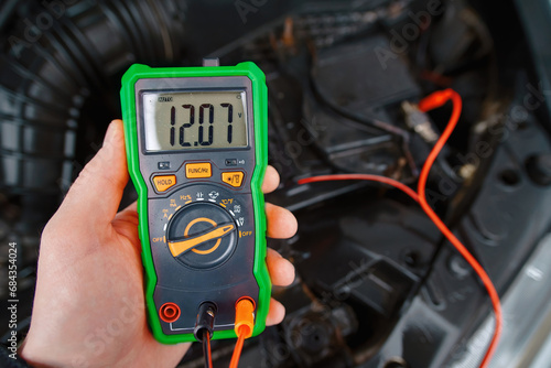 Check car battery with voltmeter. Man testing car electrical system including battery, alternator for winter season. Multimeter with voltage range measurement to check up voltage level. Low voltage