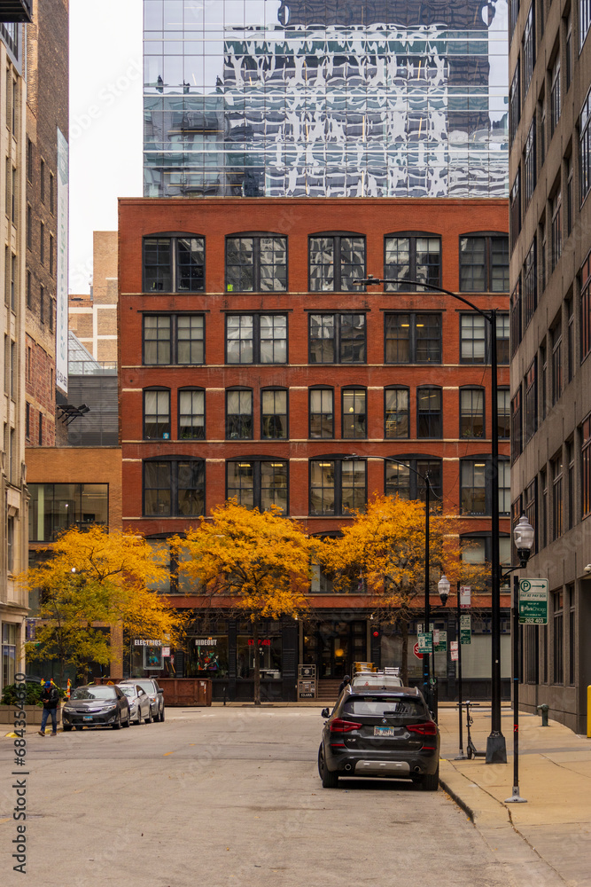 A gorgeous autumn landscape along a narrow street with parked cars, office buildings and skyscrapers and people walking and beautiful autumn trees on a cloudy day in Chicago Illinois USA A gorgeous autumn landscape along a narrow street with parked cars, office buildings and skyscrapers and people walking and beautiful autumn trees on a cloudy day in Chicago Illinois USA