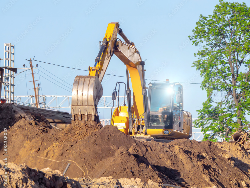 Obraz premium A yellow excavator works on a construction site. Earthworks in the city. Digging a pit