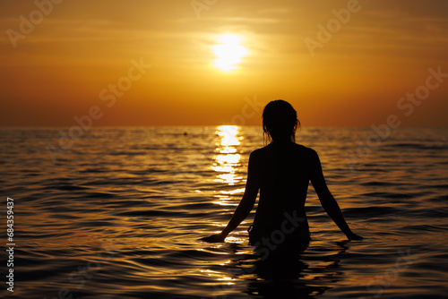 Silhouette of a girl going into the sea at sunset.