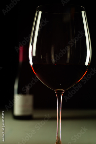 Vertica photo of a cup of red wine with a botlle behind