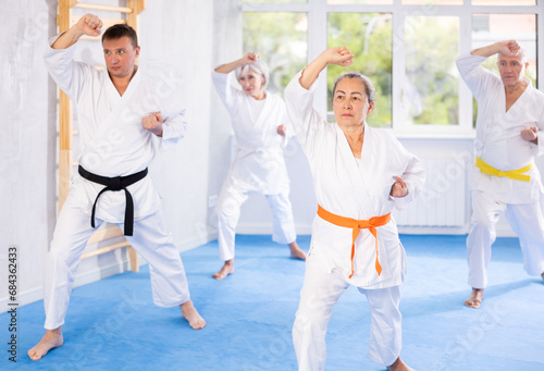 In gym, karate class senior students independently perform basic movements and repeat to hold pose, learning technique of kata. Oriental martial arts, training and obtaining black belt