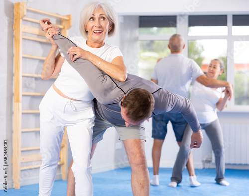 Senior woman train in pair with middle-aged coach to strike and reflect blows of enemy. Intense moment as two individuals engage in self-defense training, showcasing skill, reaction, repulse