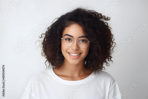 Close up studio shot of beautiful young mixed race woman model with curly dark hair looking at camera with charming cute smile while posing against white blank copy space wall for your content photo