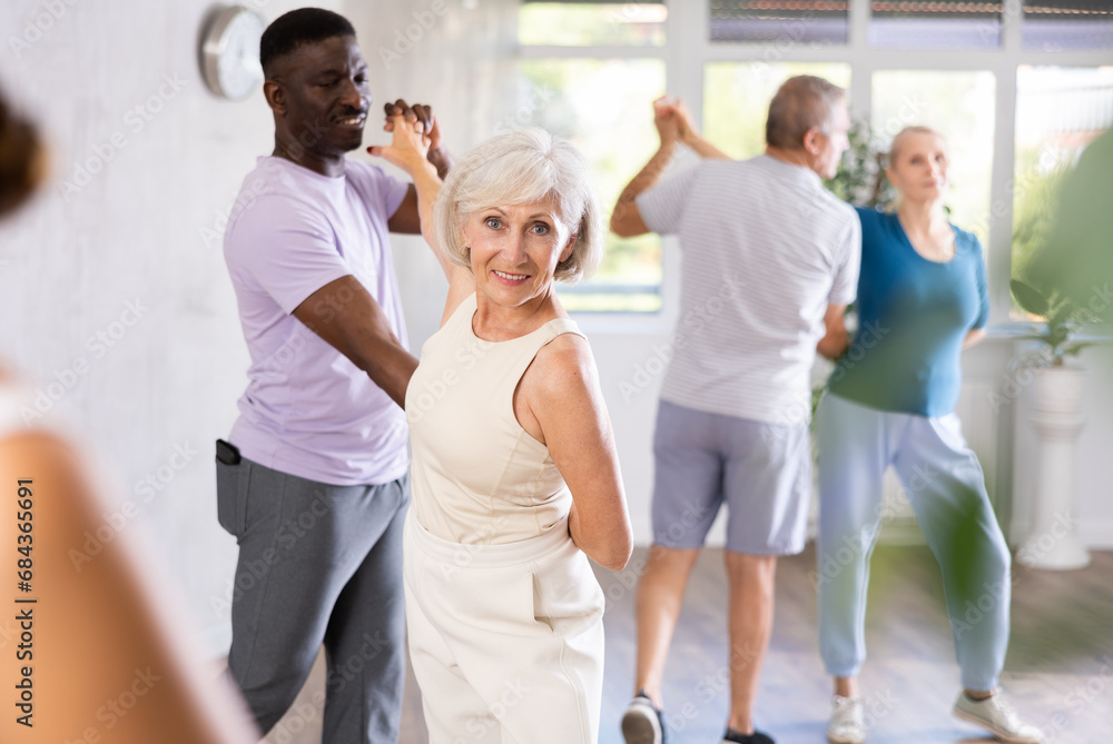 Happy smiling elderly woman enjoying impassioned merengue with african american partner in latin dance class. Social dancing concep