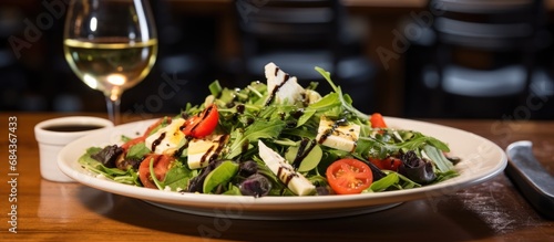 At the white marble table  a leafy green salad sat beside a steaming plate of black pasta coated in garlic-infused olive oil  accompanied by a glass of crisp white wine and a slice of creamy organic