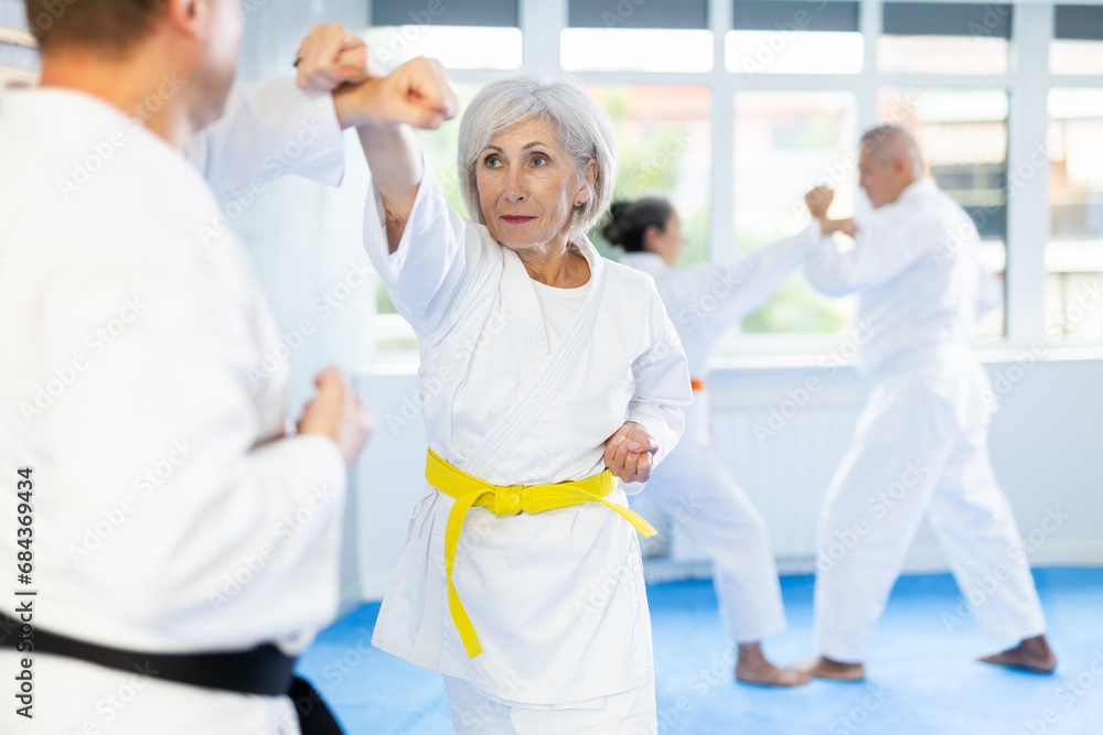 Obraz premium Elderly women and men in pairs exercising karate movements during group training