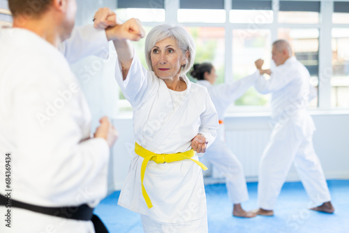 Elderly women and men in pairs exercising karate movements during group training
