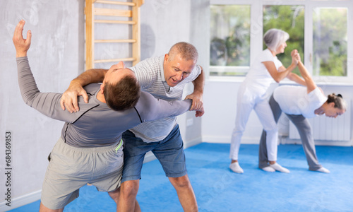 Senior man train in pair with middle-aged coach to strike and reflect blows of enemy. Intense moment as two individuals engage in self-defense training, showcasing skill, reaction, repulse