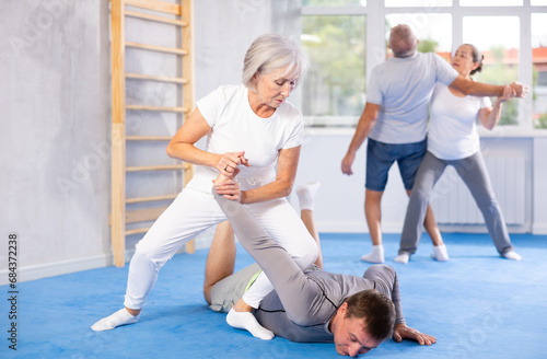 Mature woman learns how to do painful hold with trainer in the gym. Self-defense lesson