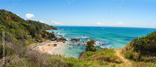 Australian coast, view from a cliff of the blue ocean and a rocky shore with a sandy beach. Small bays with volcanic rock, sunny day.