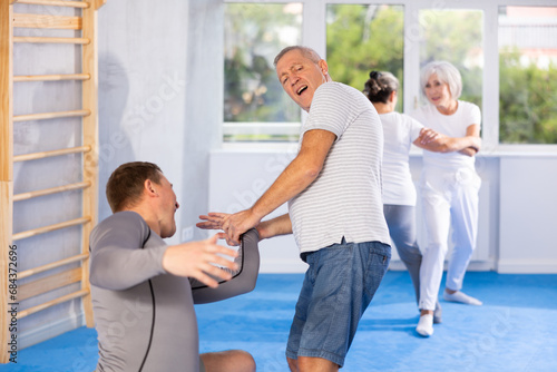 Purposeful senior male pupil clash with training manager during Krav Maga self-defense lesson, repulse charge, intensity of practice. Martial arts school, melee