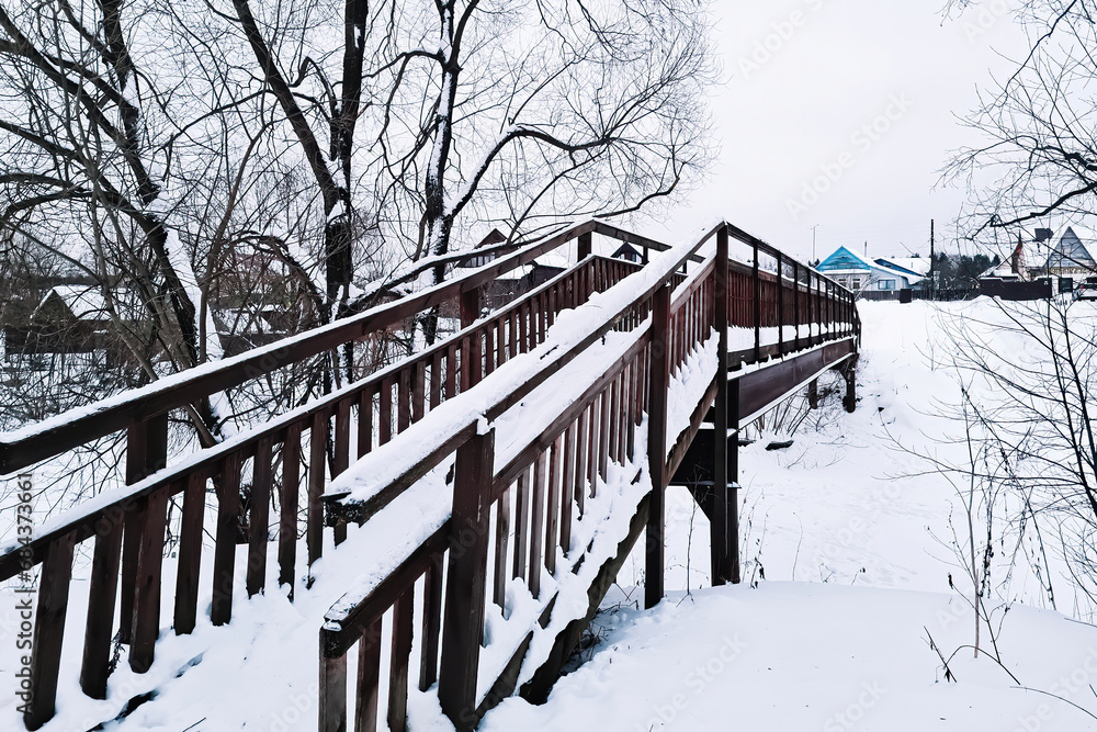 Snow-covered wooden bridge in park on winter day.