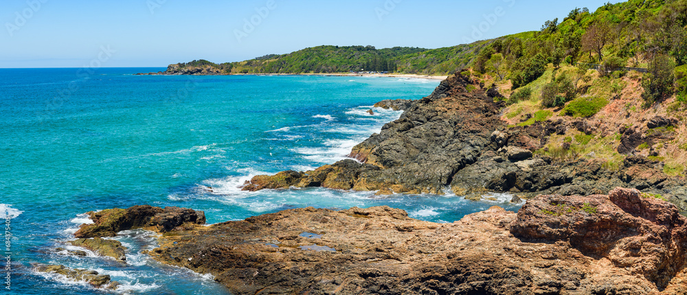 Australian coast, view from a cliff to the blue ocean with a rocky shore on a sunny day. Sea landscape, waves crashing on volcanic rocks at the shore.