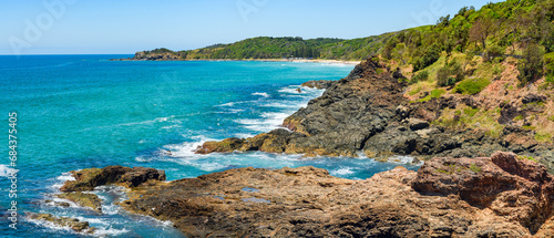 Australian coast, view from a cliff to the blue ocean with a rocky shore on a sunny day. Sea landscape, waves crashing on volcanic rocks at the shore.
