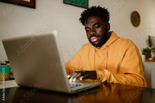 A focused serious freelancer is sitting at home and typing on a laptop at night.