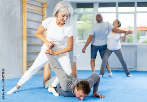 Senior woman train in pair with middle-aged coach to strike and reflect blows of enemy. Intense moment as two individuals engage in self-defense training, showcasing skill, reaction, repulse