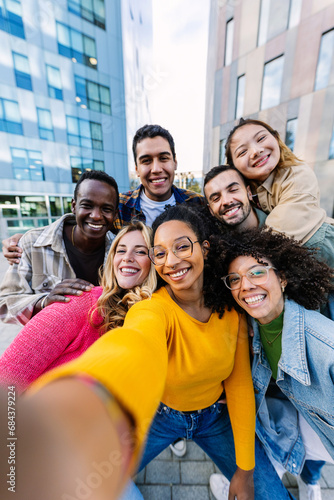 Young adult diverse friends smile at phone camera on selfie group portrait. Teenage community concept with joyful millennial students having fun together at city street. © Xavier Lorenzo