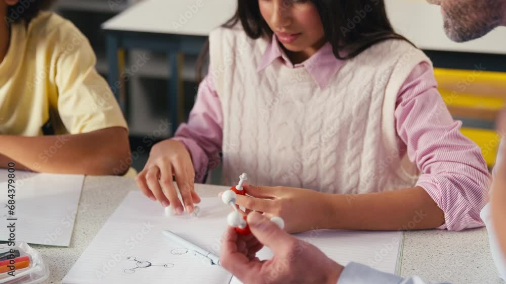 Male secondary or high school teacher helping female high school student to build model of molecule or atom in science class - shot in slow motion Male secondary or high school teacher helping female high school student to build model of molecule or atom in science class - shot in slow motion