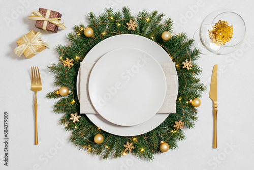 Christmas table setting with golden decorations and empty beige plate on white background. New Year table setting. Top view, flat lay.