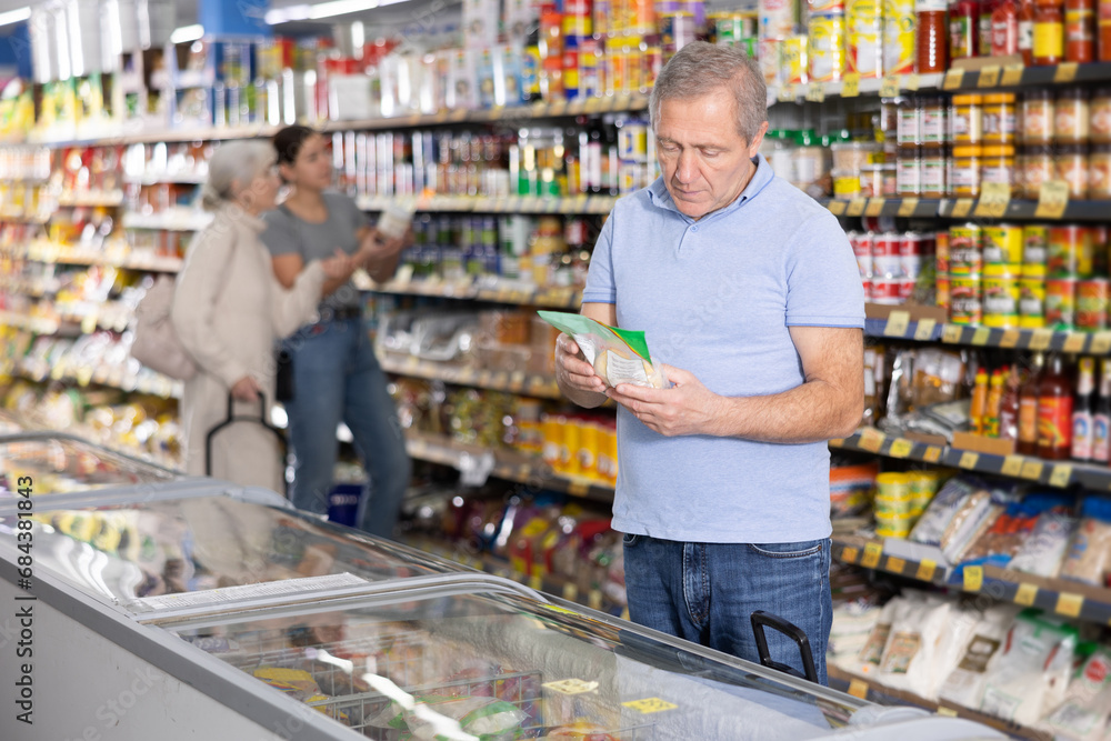 Positive mature man shopping in supermarket, choosing frozen convenience food