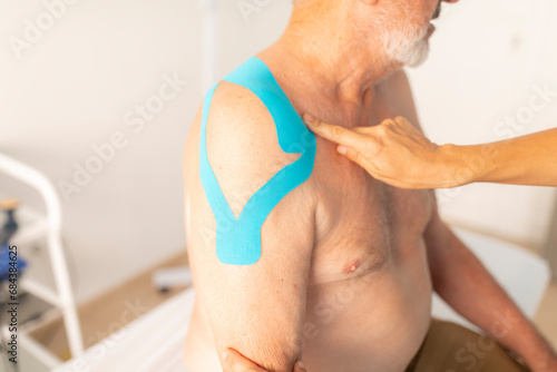 A female physiotherapist cheks the neuromuscular bandage or kinesiology tape from the shoulder of her patient, an older man photo