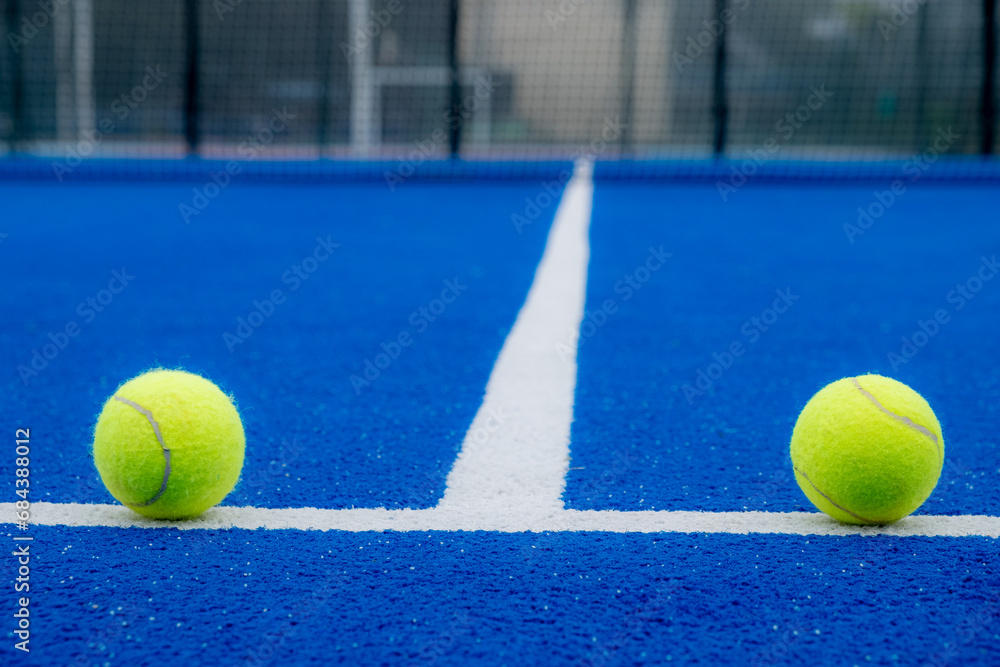 two balls on the baseline of a blue paddle tennis court