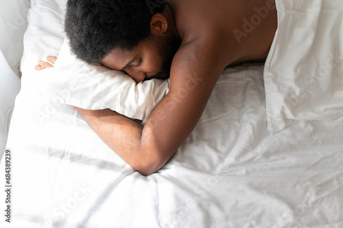 Young African American man sleeping soundly in his comfortable bed at home, lying on stomach, hugging a pillow photo