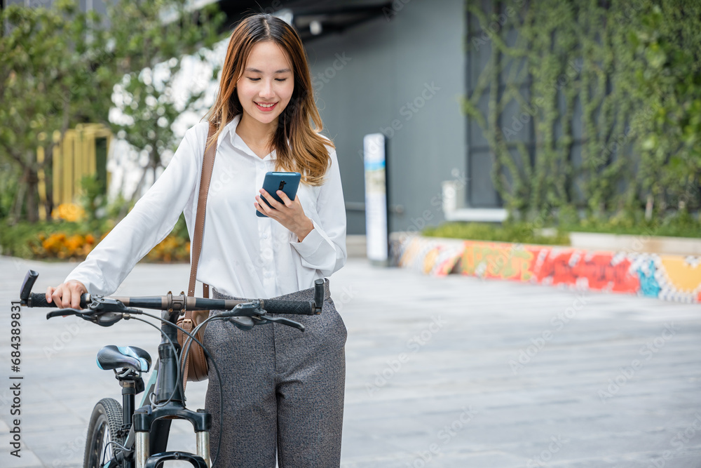 Asian businesswoman standing on city street building with bicycle holding smart mobile phone, lifestyle smiling young woman commute with her bicycle and use smartphone at urban for work social media
