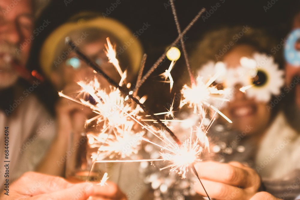 group of four people enjoying new year night celebrating with sparklers in the middle and looking at the camera - adults having fun together - obrazy, fototapety, plakaty 