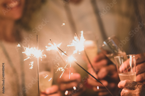group of four people having fun and enjoying holding glasses of champagne and sparklers celebrating the happy new year together