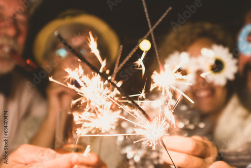 group of four people enjoying new year night celebrating with sparklers in the middle and looking at the camera - adults having fun together photo