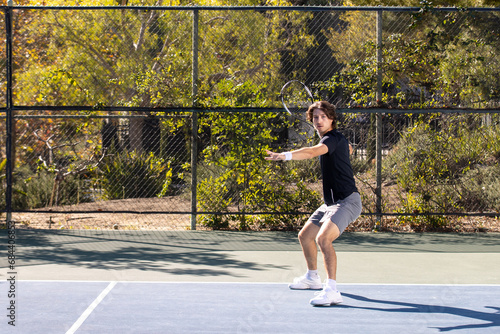 Active tennis player playing a game on an outdoor court. The man is wearing gray shorts and a black tee shirt holding a racquet.  photo