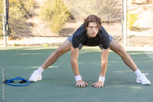 Adult male tennis player warming up and stretching before a match on the court. The man is athletic and fit ready for the action of the game.  photo